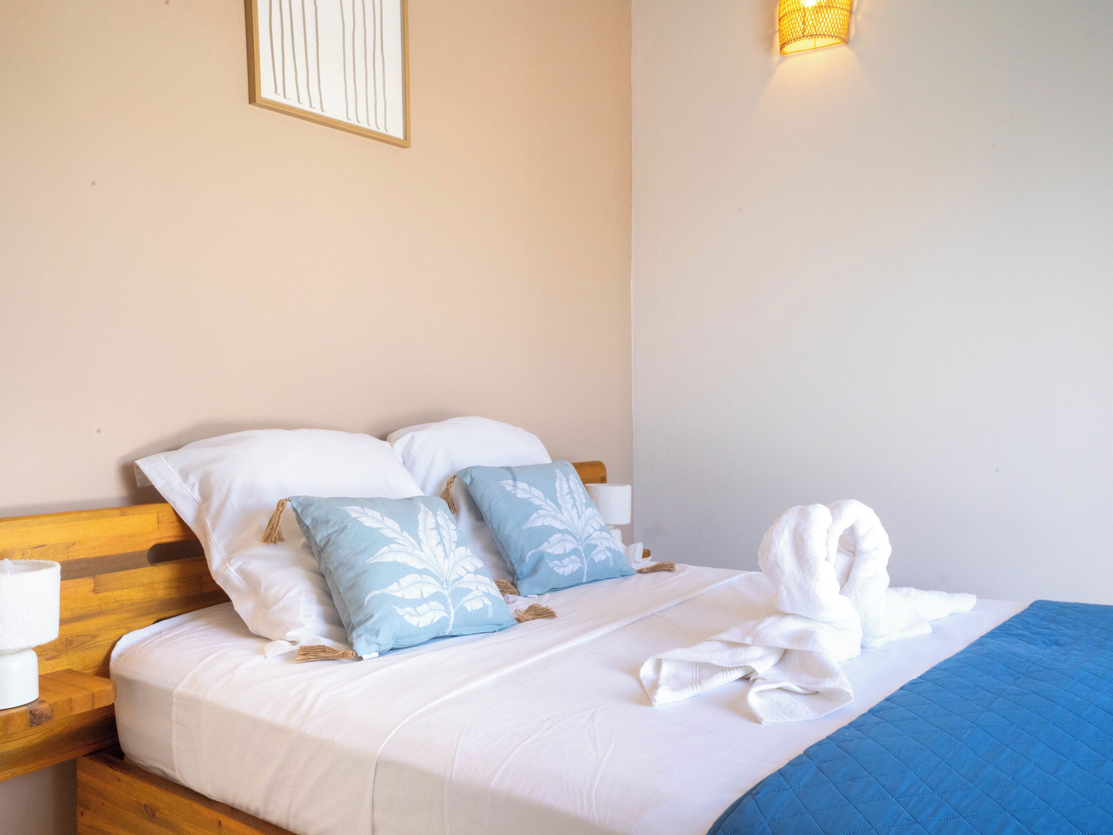 Un lit bien fait, avec des oreillers blancs et bleus, une couverture bleue et une robe blanche posée sur le lit.