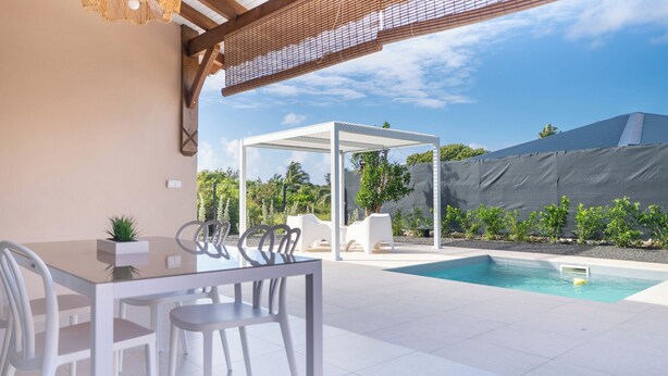 Ein moderner Essbereich im Freien mit Pool, weißer Möbel und einer Pergola.