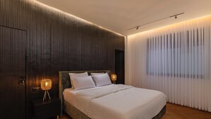 Een moderne slaapkamer met een groot bed, donker houten paneelbekleding en een groot raam met dunne gordijnen.