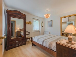 A bedroom with a wooden bed, a large mirror, a dresser, a chair, and a window with a view. - Catherine by Interhome (Pellizzano)