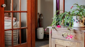 Een houten deur met glaspanelen, een bed met streepjesbeddengoed en een bloeiende kamerplant in een pot op een houten dressoir.