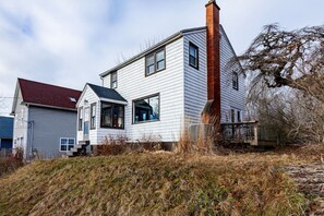 A two-story house with a red brick chimney, white siding, and a red roof.