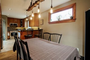 A modern kitchen with wooden cabinets, a dining table with chairs, and pendant lighting.