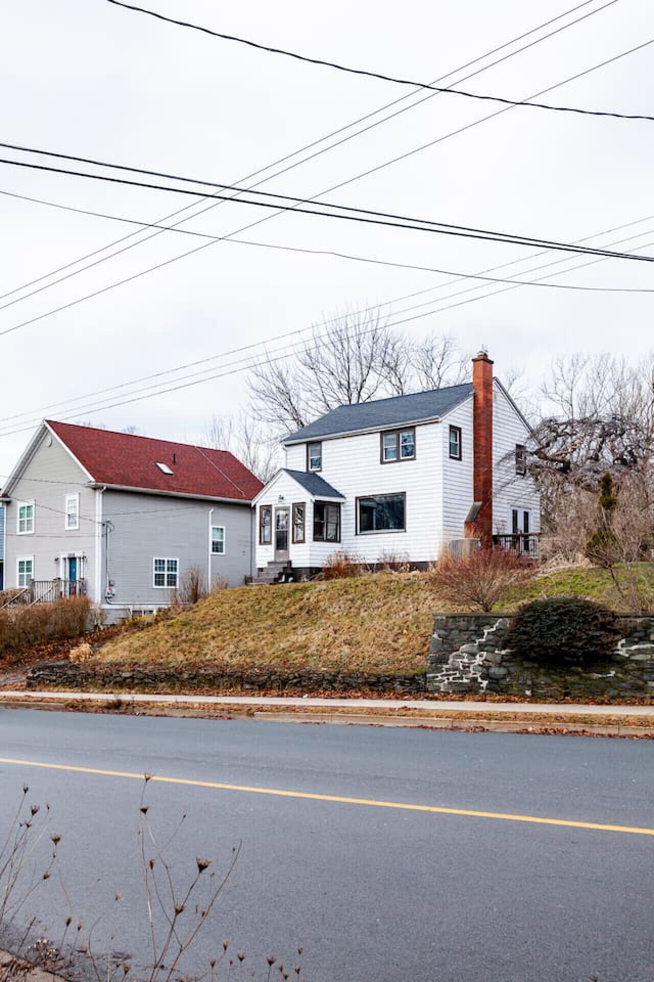 A residential street with two houses, one with a red roof and another with a white exterior and a red chimney.