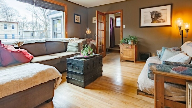 Een gezellige woonkamer met een bank, een houten dressoir en een bankje. Er is een raam met uitzicht op gebouwen.