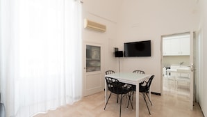 A room with a dining table, chairs, a TV, and a kitchen area visible through an open door. - Casa Argento by Monholiday (Monopoli)