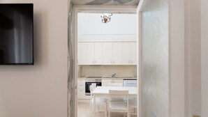 A kitchen with white cabinets, a dining table with chairs, and a TV mounted on the wall. - Casa Argento by Monholiday (Monopoli)