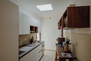 Une cuisine étroite avec des meubles blancs, une table en bois et une lucarne.