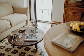 Un salon chaleureux avec un canapé beige, une table basse ronde sur laquelle se trouve un magazine, un saladier rempli de fruits et un meuble en bois.