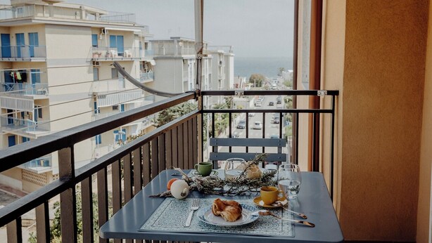 Un balcón con una mesa dispuesta para el desayuno, con vistas a la ciudad y al mar.