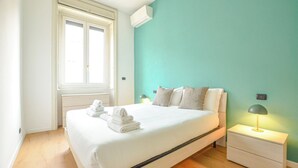 A bedroom with a bed, two bedside lamps, a window, and an air conditioning unit. - Flatsharing - Scarlatti - 2 camere (Milan)