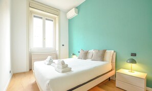A bedroom with a bed, two bedside lamps, a window, and an air conditioning unit. - Flatsharing - Scarlatti - 2 camere (Milan)