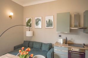 Ein Hotelzimmer mit einem Bett, einem Schreibtisch, einer Lampe, einem Strauß Tulpen und gerahmten Pflanzenbildern an der Wand.