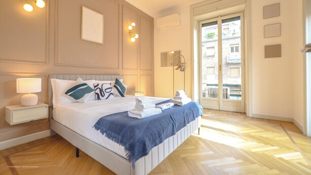 A hotel bedroom with a bed, bedside table, lamp, wall art, and a view of the outside. - Flatsharing - Scarlatti - 3 camere (Milan)