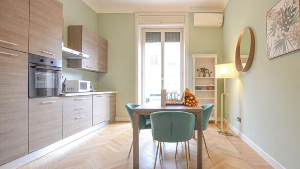 Eine moderne Küche mit integrierten Geräten, ein Essbereich mit Tisch und Stühlen und ein Blick ins Freie durch eine Tür.