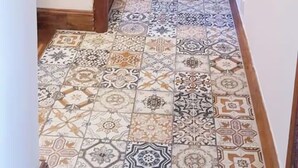 Un passadís amb una escala de fusta, rajoles de terra estampades i una porta de fusta.