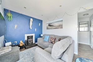 A living room with a blue accent wall, a fireplace, a grey sofa, and a painting of a boat. - 3 Bedrooms Sleeps 6 Spacious Chalet Log Burner (Bridlington)