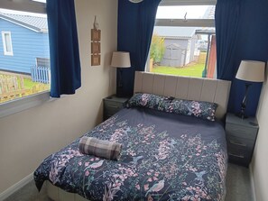 A bedroom with a bed, two bedside tables, a window with curtains, and a view of the outside. - 3 Bedrooms Sleeps 6 Spacious Chalet Log Burner (Bridlington)