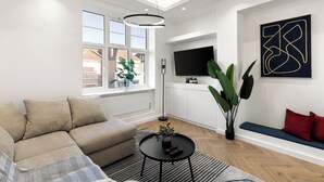 Een moderne woonkamer met een hoekbank, een ronde salontafel en een groot raam met uitzicht op gebouwen.