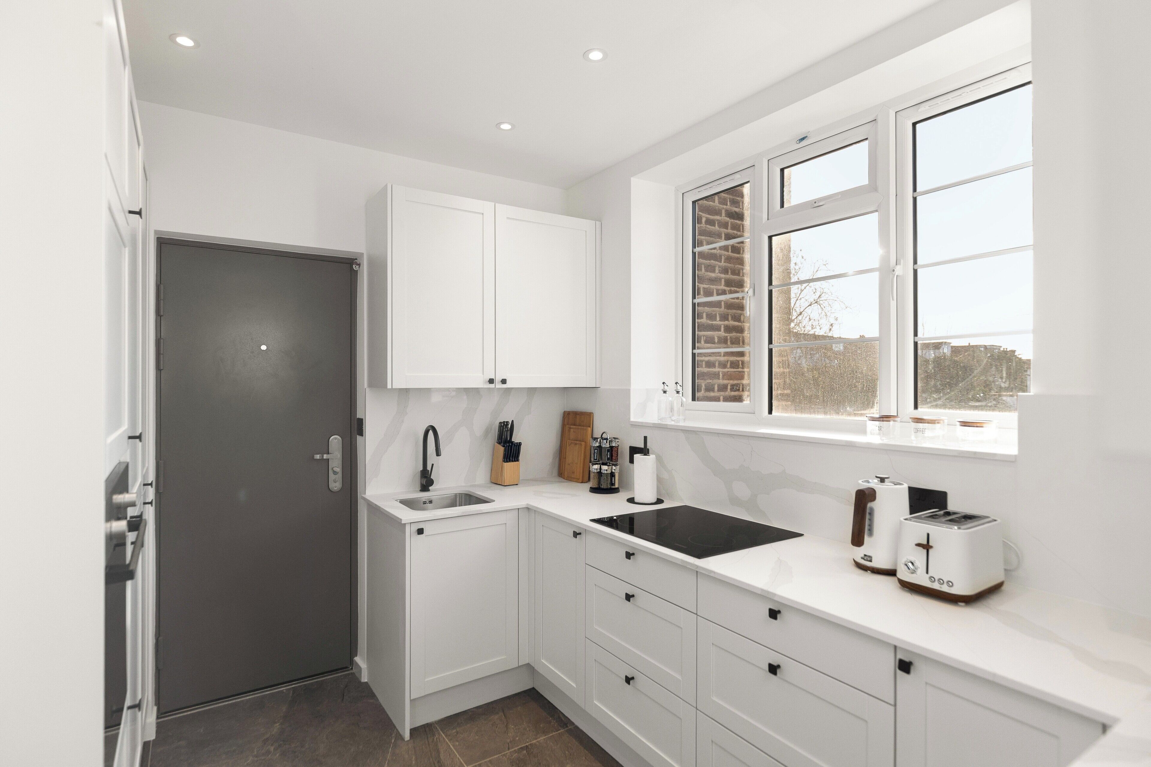 A modern kitchen with white cabinetry, a black countertop, a window with a brick pattern, and a view outside.