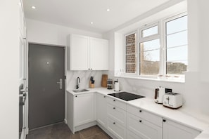 A modern kitchen with white cabinetry, a black countertop, a window with a brick pattern, and a view outside. - Apartment - Sleeps 8 - Golders Green 10 mins (London)