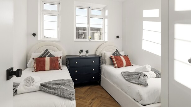 Een slaapkamer met twee bedden, een ladekast en twee ramen.