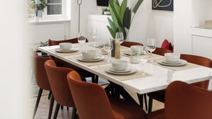 Een eettafel, gedekt met witte borden, kommen en wijnglazen, omringd door oranje stoelen.
