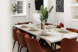 A dining table set with white plates, bowls, and wine glasses, surrounded by orange chairs. - Apartment - Sleeps 8 - Golders Green 10 mins (London)