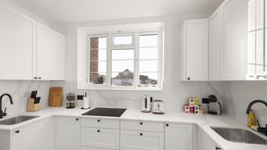 Een moderne keuken met witte kasten, een raam, een spoelbak en een aanrecht met verschillende apparaten en keukengerei.