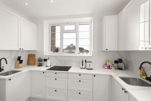 A modern kitchen with white cabinetry, a window, a sink, and a countertop with various appliances and utensils. - Apartment - Sleeps 8 - Golders Green 10 mins (London)