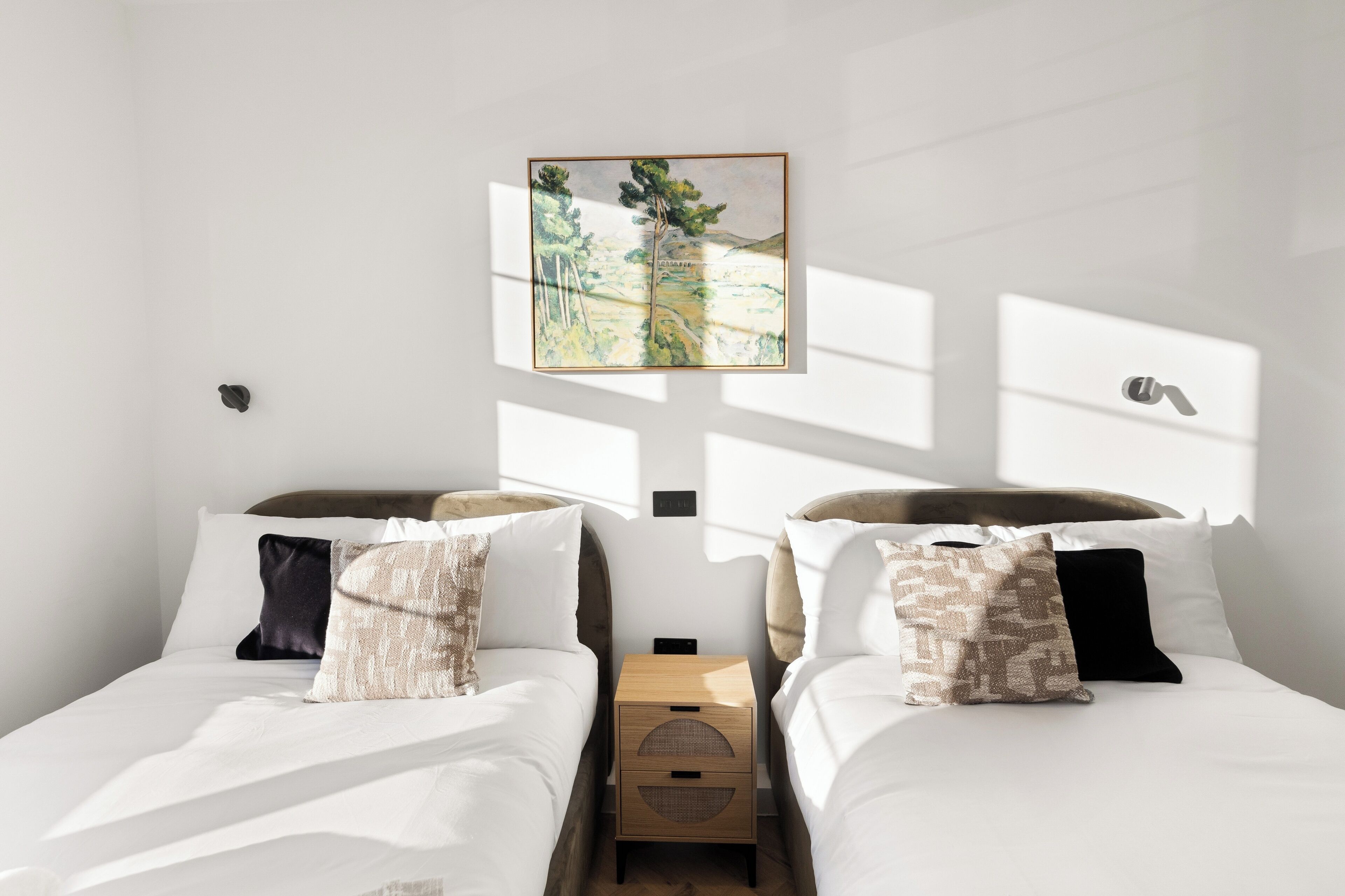 A bedroom with two beds, a nightstand, and a framed picture on the wall.