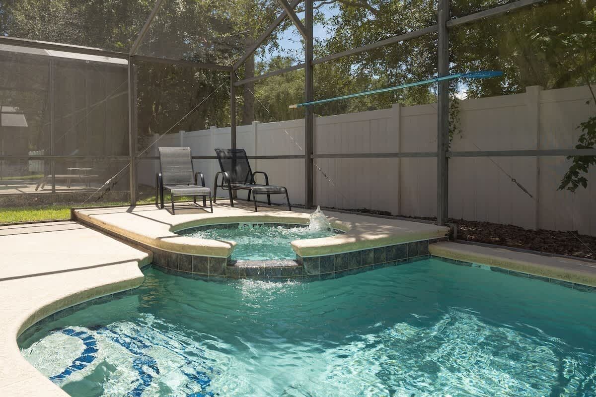 A swimming pool with a hot tub, surrounded by a covered patio area with chairs.