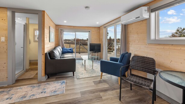 Un salon moderne avec un canapé, un fauteuil bleu, une petite table et un téléviseur.