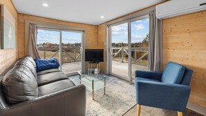 Un salon moderne avec un canapé en cuir, un fauteuil bleu, une table basse en verre et un téléviseur à écran plat.