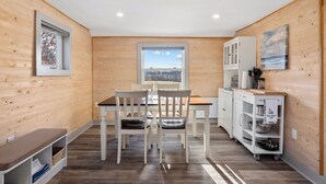 Une cuisine compacte aux murs en bois, une table à manger avec des chaises, une fenêtre donnant sur un beau paysage et un meuble blanc avec un chariot à plateaux.