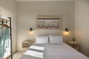 Ein Schlafzimmer mit einem großen Bett, zwei Nachttischen, einem Wandbild und einem Kleiderständer mit Handtüchern.