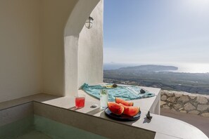 Een balkon met uitzicht op het landschap, een tafel met een bord watermeloen, een glas rode drank en een glas witte drank.