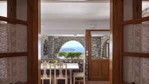 Vista a través de un marco de madera hacia un cuarto con pared de piedra, una mesa blanca y sillas.