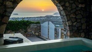Un arco de piedra que da paso a una piscina con vista al atardecer.