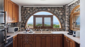 Una cocina con armarios de madera, una pared de piedra, horno empotrado, microondas y un ventanal con vistas al océano.