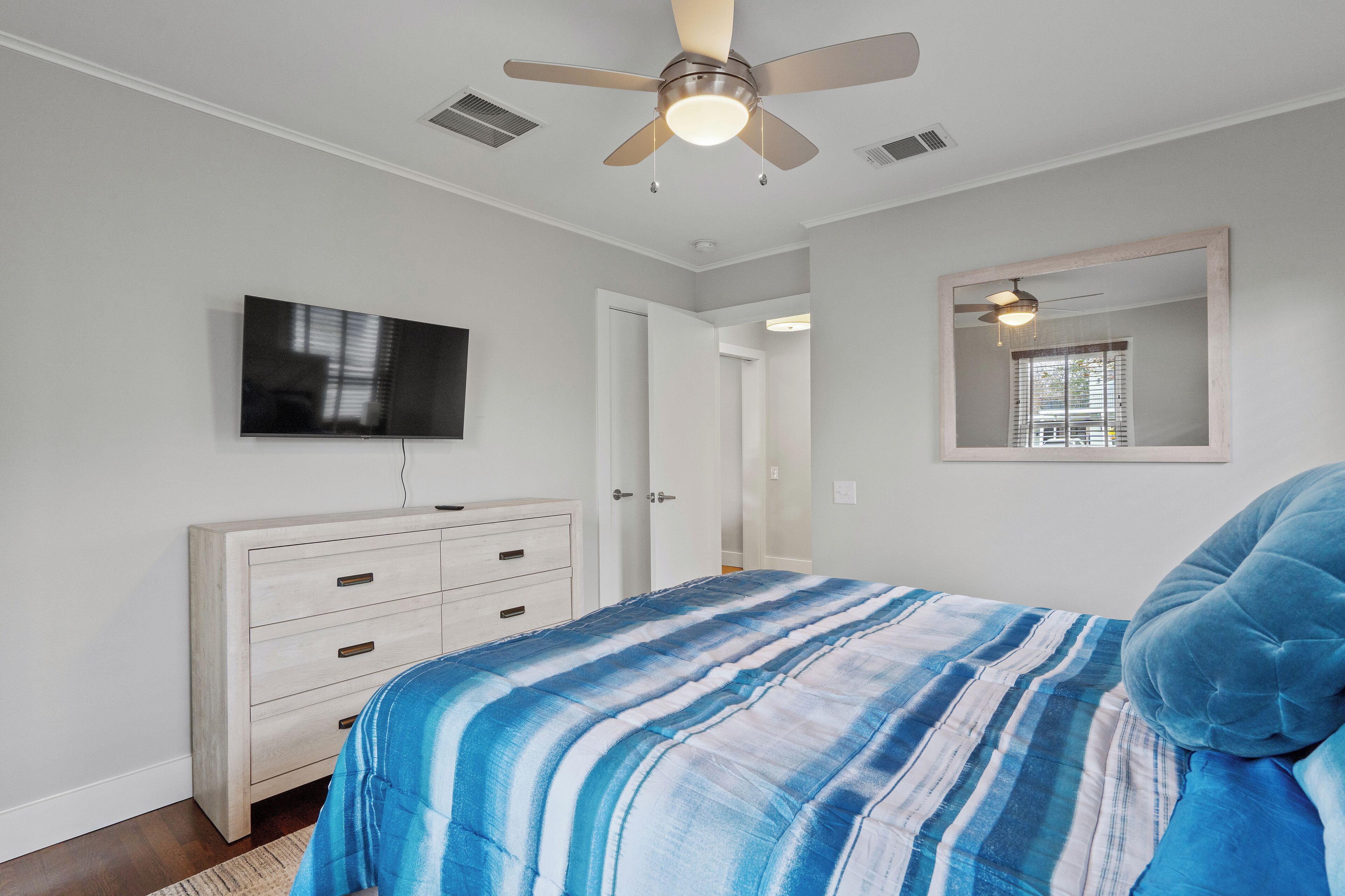 A bedroom with a bed, a ceiling fan, a TV, a dresser, and a mirror.