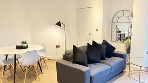 Una sala de estar moderna con un sofá gris, sillas blancas, una mesa redonda y una lámpara de pie.