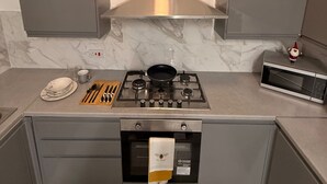 Eine moderne Küche mit Gasherd, Mikrowelle und kleinem Backofen. Auf der Arbeitsplatte liegen ein Holzer Schneidebrett und Küchenutensilien.