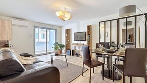 Een moderne woonkamer met een bank, een eettafel met stoelen, een televisie en een groot raam.