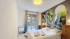 Een slaapkamer met een bed, een dressoir, een raam met gordijnen en uitzicht op groen.