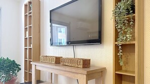 Een woonkamer met een houten tv-meubel, een flatscreen televisie, een kamerplant en een rieten mand.