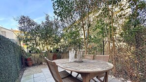 Een ronde houten tafel met vier stoelen, omringd door een tuin met verschillende planten en bomen.