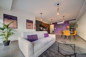 A modern living room with a sofa, a glass coffee table, and a dining area with chairs and a table. - Kuya Suite No.1 / Central / Terrace (Swieqi)