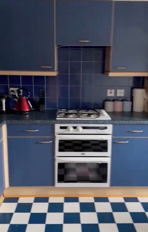 A kitchen with blue cabinets, a gas stove, an oven, and a checkered floor. - Aberdeen City Escape Apartment (Aberdeen)