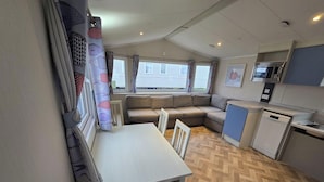 Une petite cuisine équipée comprenant un four à micro-ondes, un four et un lave-vaisselle. Une petite table à manger et deux chaises sont placées devant un canapé.
